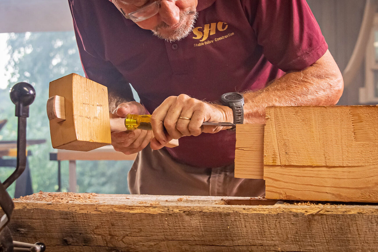 Craftsman chiseling a reclaimed wood barn beam