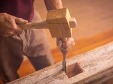 man with wooden hammer chiseling a hole on a reclaimed wood beam 