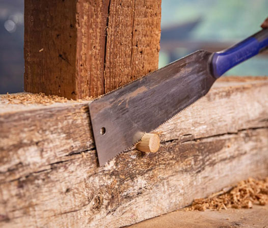 using a hand tool to cut a timber framed peg
